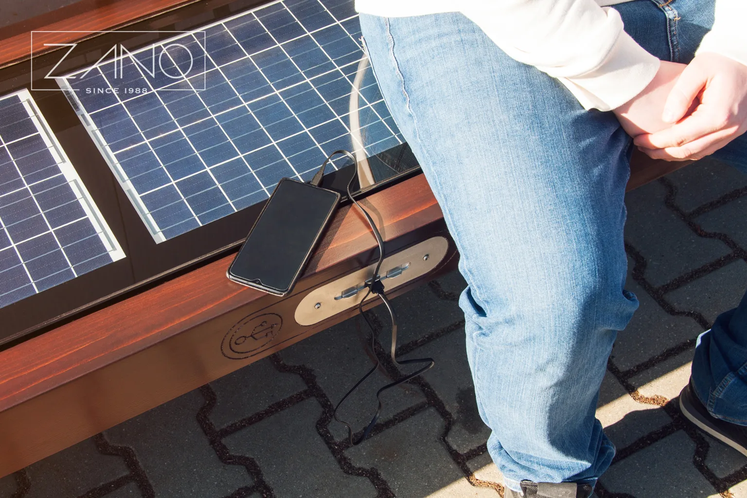Telefono įkrovimas naudojant „Szczepańska“ Saulės energijos suoliuką, pagamintą „ZANO Smart City“